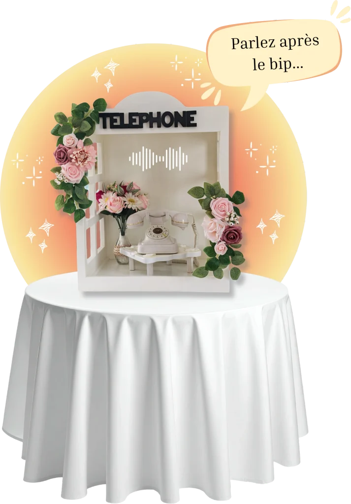 Cabine téléphonique vintage de table blanche décorée de fleurs roses, avec un téléphone rétro à l’intérieur permettant d'enregistrer des messages avec une bulle 'parlez après le bip"
