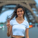 Smiling young woman poses with peace sign in front of the Eiffel Tower in Paris, France.